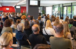 Auf dem Bild zu sehen sind Menschen, zumeist Lehrkräfte, die auf dem Fachtag der BiSS-Akademie NRW in Köln einem Vortrag folgen.