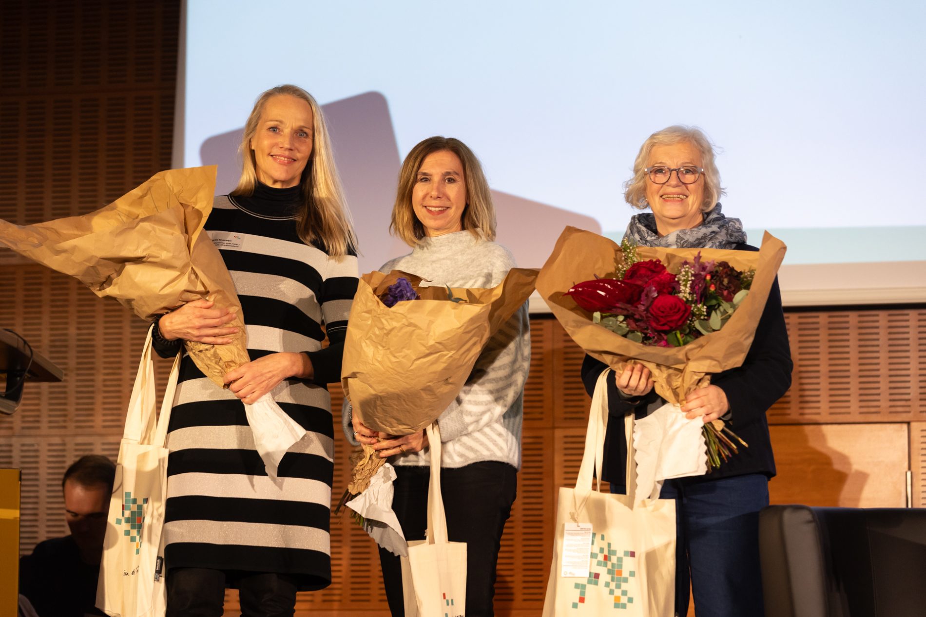 Das Bild zeigt drei Multiplikatorinnen mit Blumenstrauß auf der Bühne der BiSS-Transfer-Jahrestagung 2023, die für ihre Leistung im Rahmen von BiSS-Transfer geehrt werden.