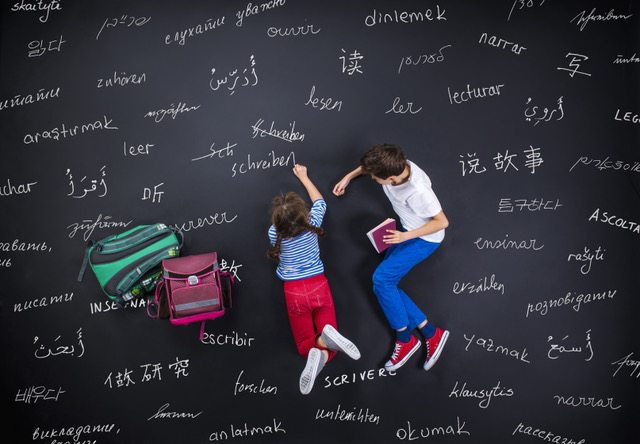 Das Bild zeigt zwei Kinder, die in verschiedenen Sprachen Wörter auf eine große Tafel schreiben. Das Foto zeigt das Thema Mehrsprachigkeit. Das Foto stammt von AdobeStock, Halfpoint.